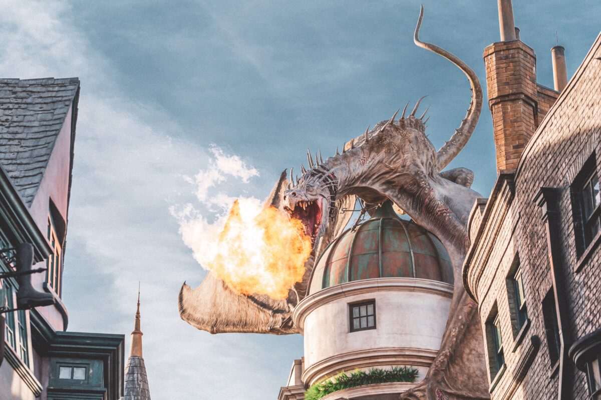 A dragon, landed atop a tower, breathing fire towards the viewer.